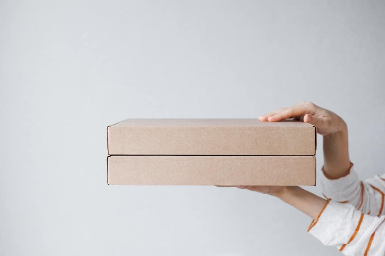 women's hands hold cardboard boxes on a gray background. food and drink delivery. biodegradable packaging. Service for ordering food and clothing. cardboard pizza and pie box