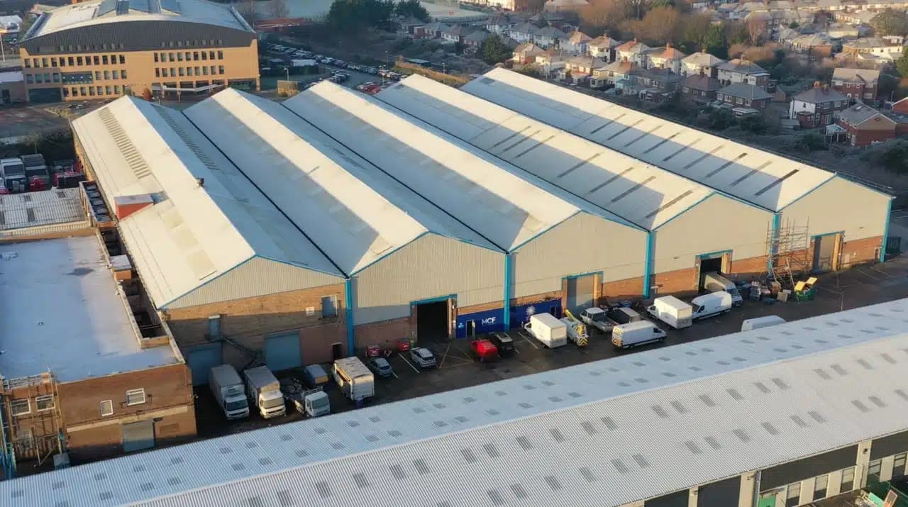 Aerial view of a large multi-bay fulfilment warehouse with loading bays and delivery vehicles parked outside.