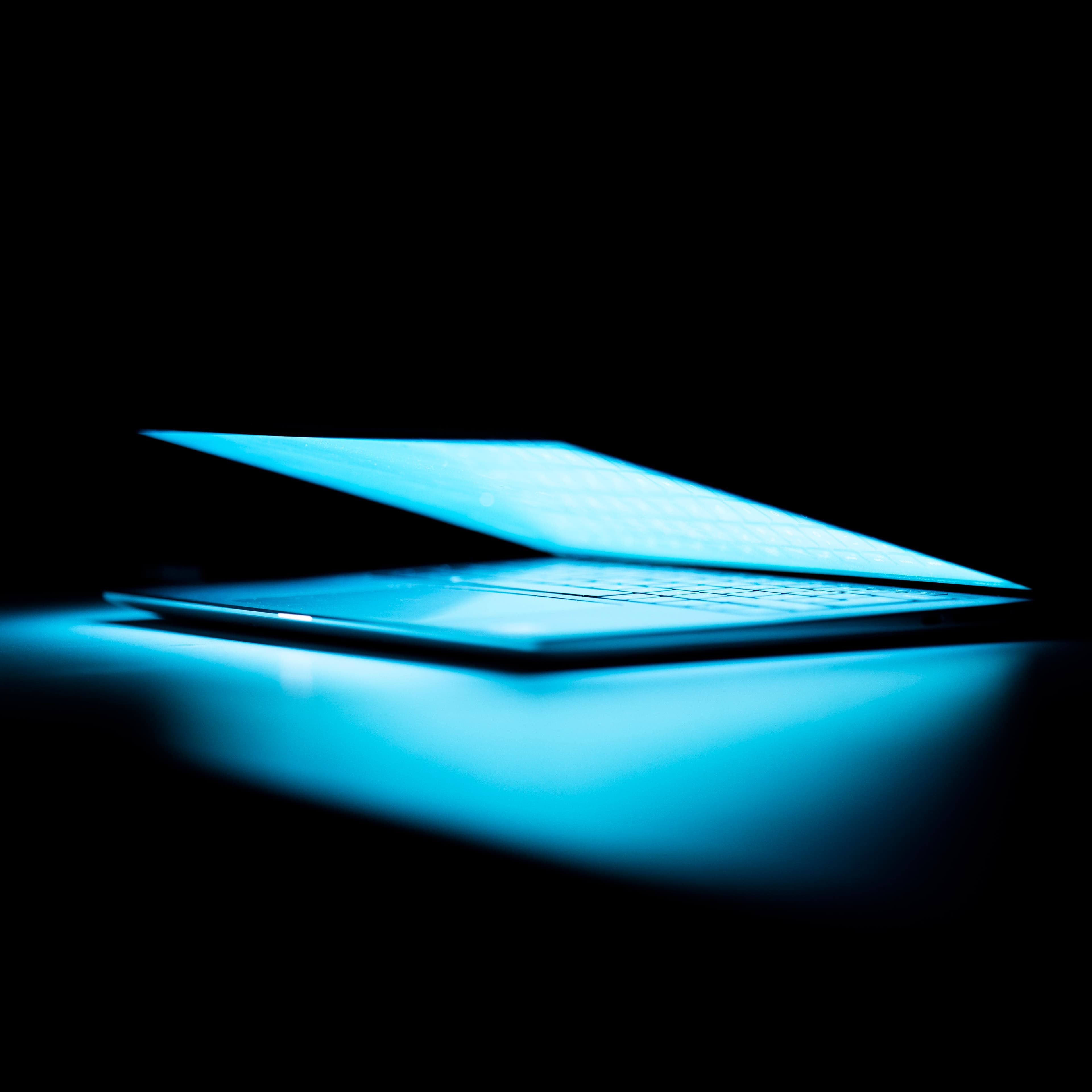 A closeup shot of a half-open laptop shining light on a dark table
