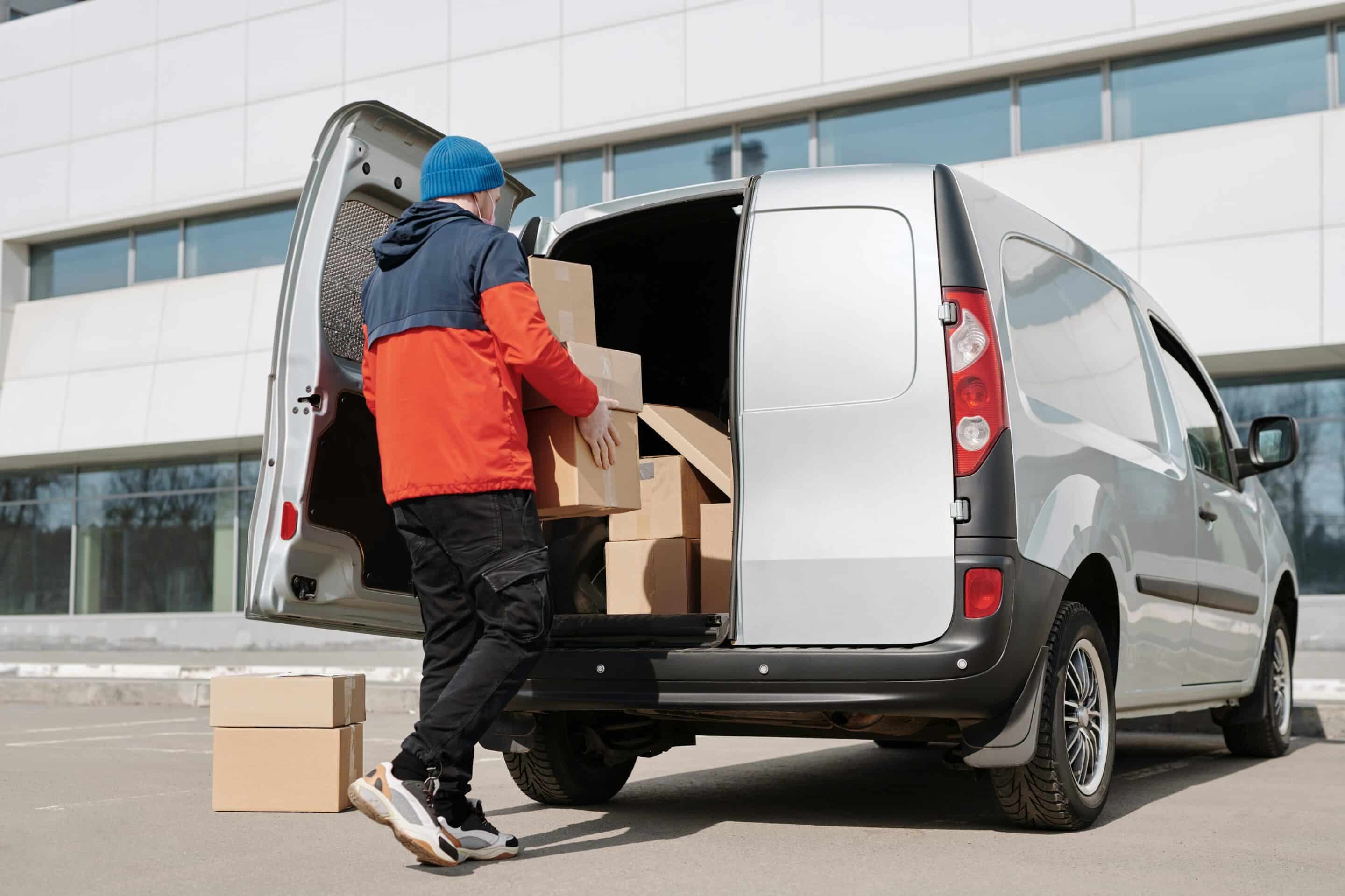 Delivery driver loading cardboard parcels into the back of a van for dispatch from a fulfilment warehouse.