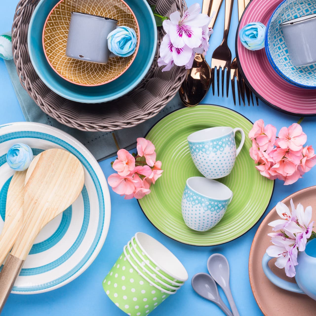 Tableware dish set on blue pastel background with flowers. Flat lay